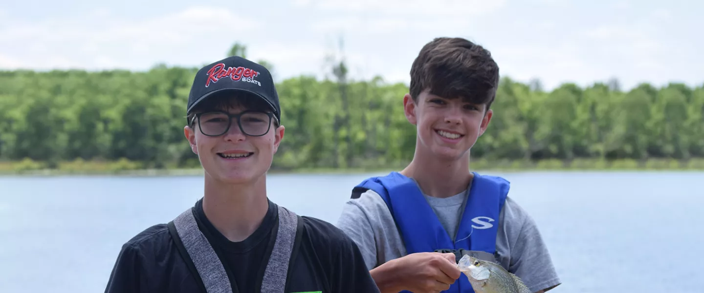 Camper holding a fish while standing near another camper