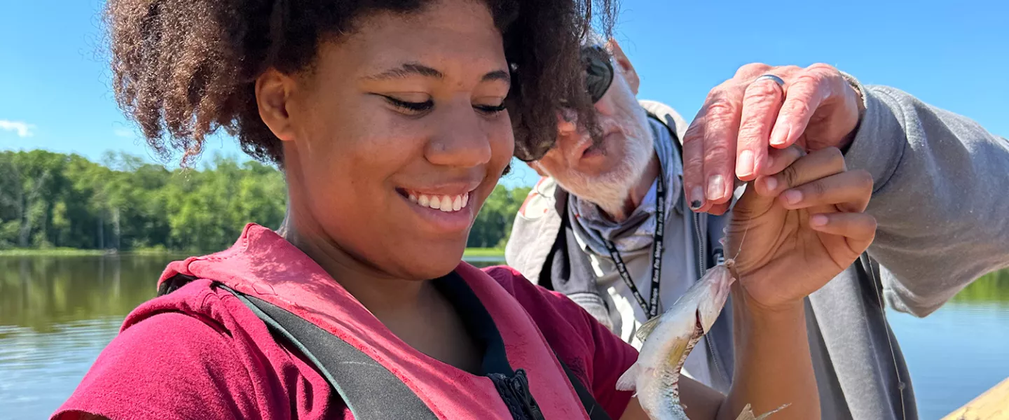 camper holding fish while staff helps