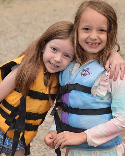 two campers in life jackets side hugging and smiling